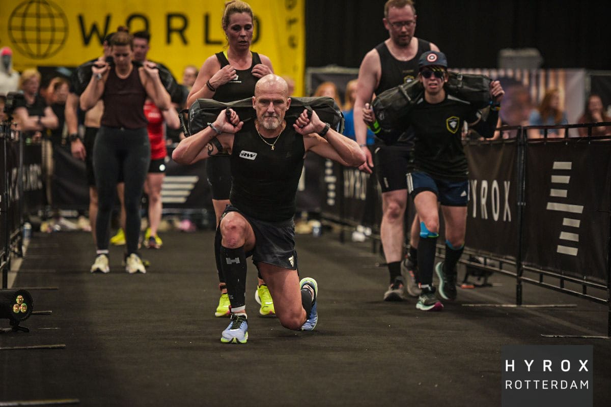 sporter met zwarte compressie tubes tijdens een hyrox wedstrijd bij de sandbag lunges