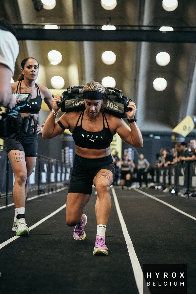 sporter met witte enkelsokken tijdens een hyrox wedstrijd bij de sandbag lunges
