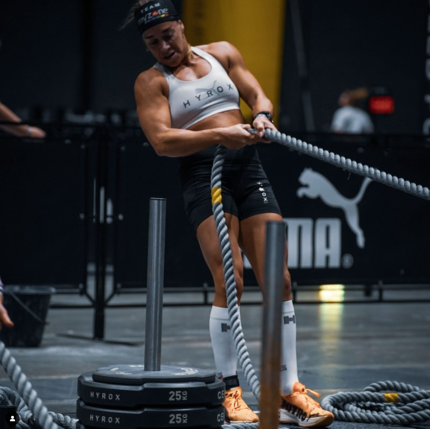 sporter tijdens een hyroxwedstrijd terwijl ze compressiekousen draagt tijdens de sled pull