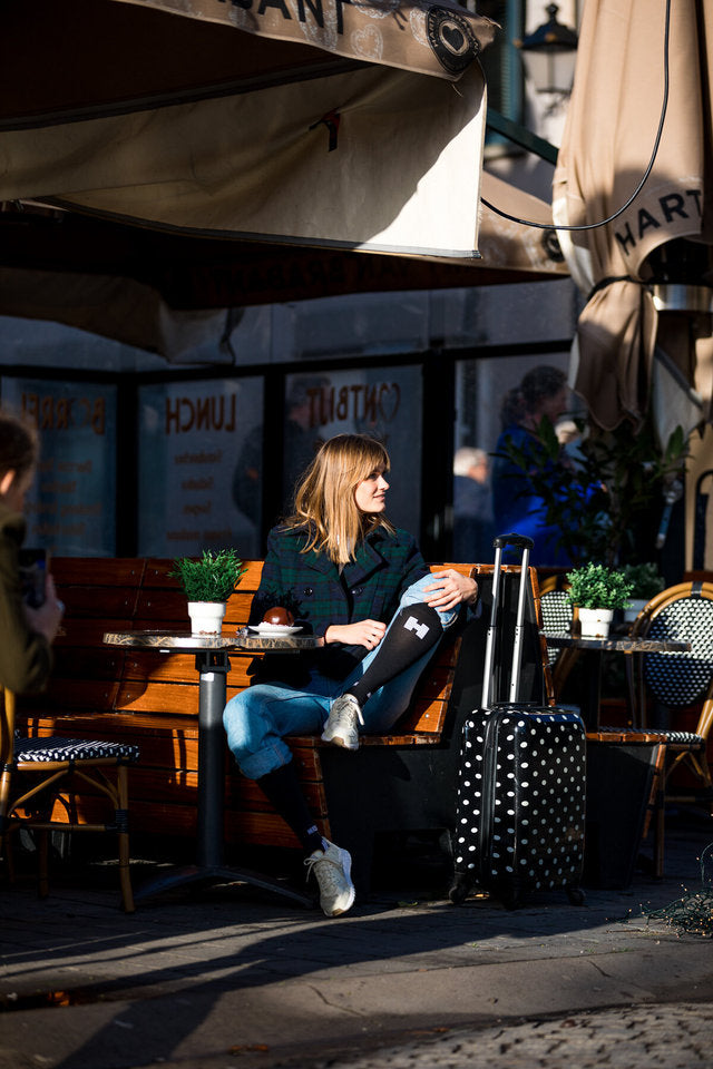 een vrouw zit op een bankje tijdens het reizen en draagt compressiekousen